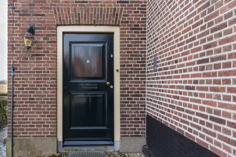 Een zwarte voordeur met een lamp in een bakstenen gevel